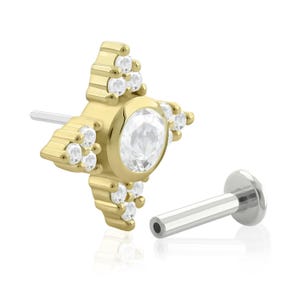 May include: Gold body jewelry with a star-shaped design and clear gemstones. The jewelry is separated into two parts: a star-shaped top and a straight post.