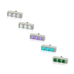 May include: Five rectangular metal body jewelry attachments, each featuring three small, round, faceted gemstones set in a row. The stones are clear, iridescent, purple, bright blue, and green, with a small metal post extending from the back.