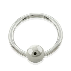 Pode incluir: Um anel circular de contas cativas feito de metal prateado polido. A peça de joalharia apresenta um aro liso e contínuo com uma única conta esférica centrada na parte inferior, mantida no lugar pela tensão da estrutura do aro.