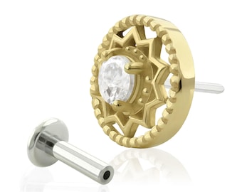 May include: A gold-toned flat back stud earring featuring a circular frame with a beaded edge and a central star-shaped cutout holding a clear, round-cut gemstone. The piece includes a separate silver-toned metal post with a flat circular base.