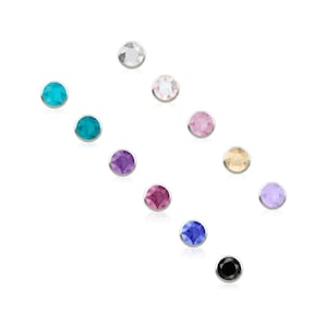 May include: A collection of eleven circular stud earrings, each featuring a single faceted gemstone set in a silver-toned metal bezel. The stones display a variety of colours including clear, turquoise, pink, purple, magenta, blue, black, and beige.
