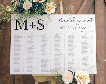 May include: A white wedding seating chart with the letters "M+S" at the top. The chart is divided into alphabetical sections and lists guest names. The chart is on a wooden easel with flowers.