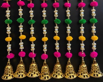 May include: Seven strands of decorative door hangings with pink, green, yellow, and white pom-poms, red and gold fabric balls, and gold bells at the bottom.