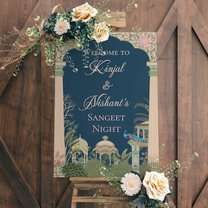 May include: A blue and gold welcome sign with an ornate design and the text "Welcome to Kinjal & Nishant's Sangeet Night". The sign is decorated with flowers and greenery.