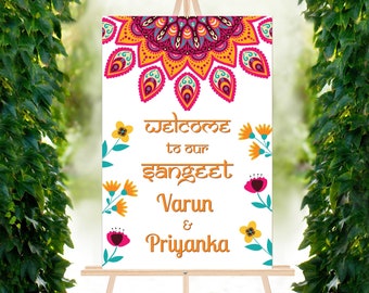 May include: A white welcome sign with a colorful mandala design at the top. The sign says "Welcome to our Sangeet Varun & Priyanka".