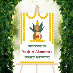 May include: A white welcome sign with yellow floral garlands, a gold pot with a green plant, and the text "welcome to Yash & Akansha's house warming".