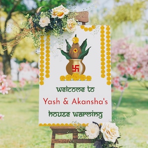 May include: A white sign with gold trim and yellow flowers welcomes guests to Yash & Akansha's housewarming. The sign features a traditional Indian pot with green leaves and a red swastika symbol.