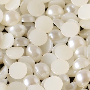 Può includere: Primo piano di un mucchio di cabochon rotondi di colore bianco perlato con retro piatto. I cabochon sono lisci e lucidi.