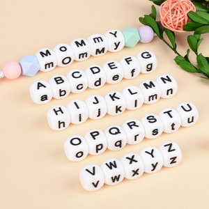 May include: White alphabet beads with black lettering. The beads are arranged in rows, starting with the letter A and ending with the letter Z. The beads are made of silicone and are perfect for teething babies.
