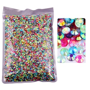 May include: A resealable plastic bag filled with a variety of iridescent, multi-colored rhinestones. The rhinestones are small and round, and they are arranged in a random pattern. A close-up image shows a smaller sample of the rhinestones.