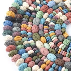 May include: A selection of lava rock beads in a range of colours, including white, black, brown, green, blue, and orange. The beads are oval shaped and have a rough, porous texture.