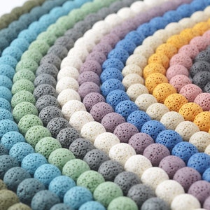 May include: A variety of colors of lava rock beads, arranged in rows. The beads are round and have a porous texture. The colors include white, gray, blue, green, purple, and orange.