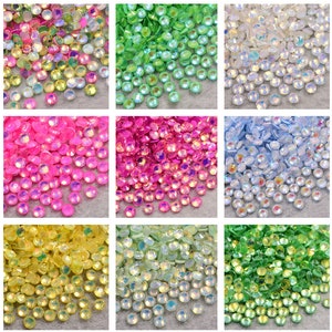 May include: Assortment of iridescent glass rhinestones in various colours, including green, blue, pink, yellow, and white. The rhinestones are small and round, with a faceted surface that reflects light.