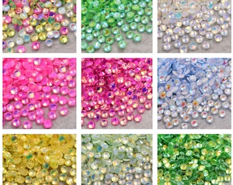 May include: Assortment of iridescent glass rhinestones in various colours, including green, blue, pink, yellow, and white. The rhinestones are small and round, with a faceted surface that reflects light.