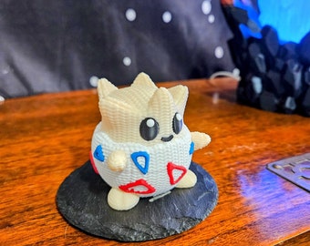 May include: A white and red 3D printed Pokemon figurine of a Snorlax, standing on a black slate base.
