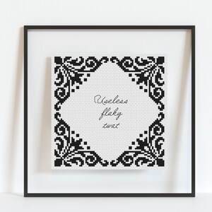 May include: Black and white cross-stitch embroidery design with a decorative frame and the text "Useless Flaky Twat" inside.
