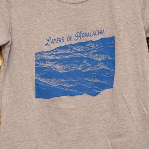 May include: A heather grey t-shirt with a blue graphic of a mountain range and the text "Layers of Appalachia".