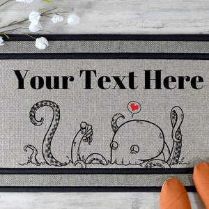 Pu&ograve; includere: Un tappetino per la porta con un bordo nero e uno sfondo grigio. Il tappetino presenta un'illustrazione in bianco e nero di un polpo con un cuore sopra la testa. Il testo "Your Text Here" &egrave; stampato in nero nella parte superiore del tappetino.