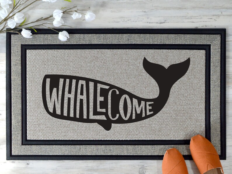 May include: A black and white doormat with a whale silhouette. The word "WHALEcome" is spelled out inside the whale's body.
