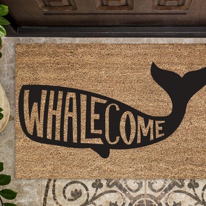 May include: A brown coir doormat with a black whale silhouette. The whale's body is formed by the word "WHALEcome" in a playful font.