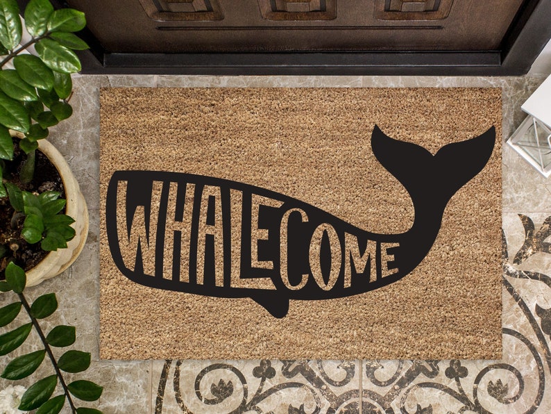 May include: A brown coir doormat with a black whale silhouette. The whale's body is formed by the word "WHALEcome" in a playful font.