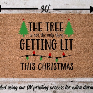以下が含まれることがあります： 茶色のココナッツ繊維のドアマットに、「THE TREE is not the only thing GETTING LIT THIS CHRISTMAS」という黒い文字が書かれています。文字の両側には、赤い星がついた緑のクリスマスツリーが2本あります。文字の下には、赤と緑の電球がついたクリスマスライトの列があります。ドアマットのサイズは、76cm x 46cmです。