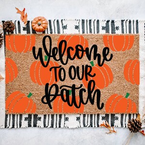 Könnte beinhalten: Ein rechteckiger Fußabtreter mit einer braunen Kokosfaseroberfläche, mit orangefarbenen Kürbisgrafiken und dem Text "Welcome To Our Patch" in schwarzer Schrift. Die Matte ist von einem schwarz-weiß gemusterten Stoff mit schwarzem Fransen umrandet.