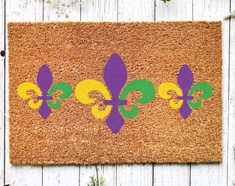 May include: A brown coir doormat with three purple, yellow, and green fleur-de-lis designs.