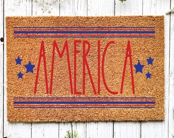 May include: A brown coir doormat with the word "AMERICA" in red lettering. The doormat has three red and blue stripes above and below the word.