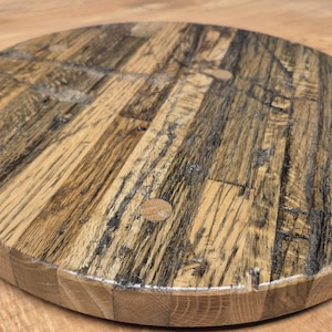 May include: Round wooden serving board with a rustic design. The board is made from reclaimed wood, featuring a mix of light and dark brown tones. The surface has a natural wood grain pattern and is approximately 12 inches in diameter.