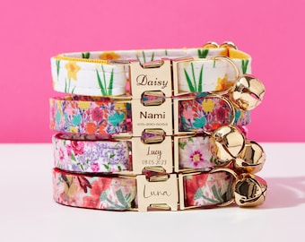 May include: Four colorful floral cat collars with gold name tags and bells. The collars are stacked on top of each other. The name tags read "Daisy", "Nami", "Lucy", and "Luna".