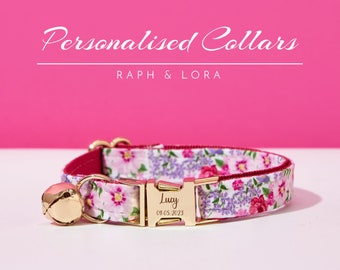 May include: A floral patterned pet collar with a gold-colored buckle and bell. The collar features a white background with pink and purple flowers. The buckle is engraved with the name "Lucy" and the date "09.05.2023". The text "Personalised Collars" is at the top.