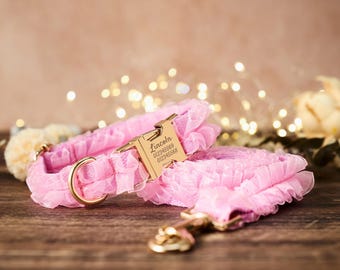 Könnte beinhalten: Rosa Hundehalsband und Leine mit Rüschendesign. Das Halsband hat eine goldfarbene Schnalle und ein Etikett mit dem Namen "Lincoln" und einer Telefonnummer. Die Leine hat einen passenden goldfarbenen Verschluss.