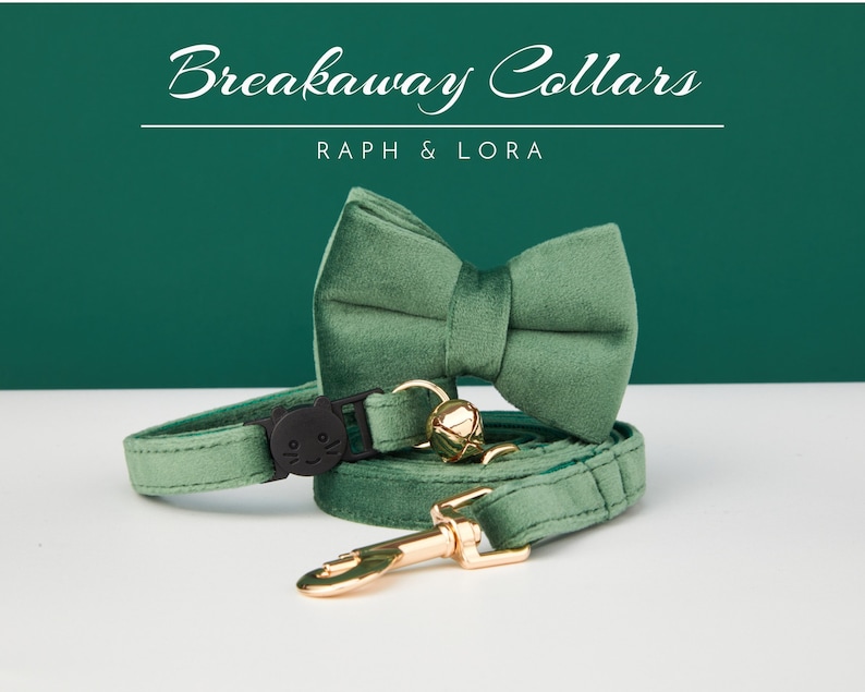 May include: A green velvet breakaway cat collar with a matching bow tie. The collar has a black safety buckle with a cat face design and a gold bell. The text "Breakaway Collars" and "Raph & Lora" is printed on a green background.