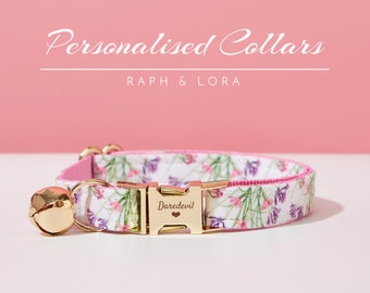 May include: A white and pink floral cat collar with a gold buckle and bell. The buckle is engraved with the word "Daredevil" and a small heart.