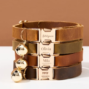 Könnte beinhalten: Vier braune Lederkatzenhalsbänder mit goldenen Schnallen und gravierten Namen: Betelgeuse, Olivia, Mila und Piper. Jedes Halsband hat eine goldene Glocke.