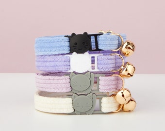 May include: Four colorful cat collars with cute cat-shaped buckles and gold bells. The collars are made of soft, textured fabric and are available in light blue, lavender, pink, and white.