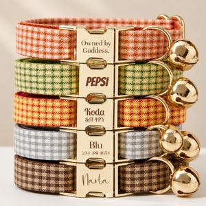 May include: A stack of five pet collars with gingham patterns in orange, green, yellow, gray, and brown. Each collar features a gold-tone metal buckle engraved with text including Owned by Goddess, PEPSI, Koda SA1 4PY, Blu 234-381-1654, and Narla.