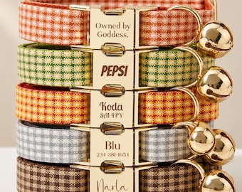 Peut inclure: Une pile de cinq colliers pour animaux avec des motifs vichy orange, vert, jaune, gris et marron. Chaque collier possède une boucle en métal doré gravée avec les textes Owned by Goddess, PEPSI, Koda SA1 4PY, Blu 234-381-1654 et Narla.