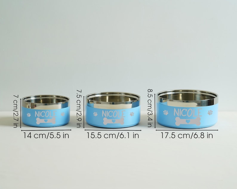 May include: Three stainless steel pet bowls with light blue bands. Each bowl has the name "NICOLE", a bone graphic, and paw prints. The bowls measure 5.5, 6.1, and 6.8 inches in diameter.