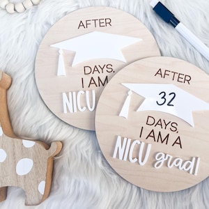 May include: Two wooden signs with a graduation cap design. The signs read "After 32 days, I am a NICU grad!" and "After days, I am NICU".