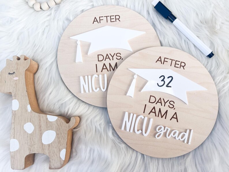 May include: Two wooden signs with a graduation cap design. The signs read "After 32 days, I am a NICU grad!" and "After days, I am NICU".