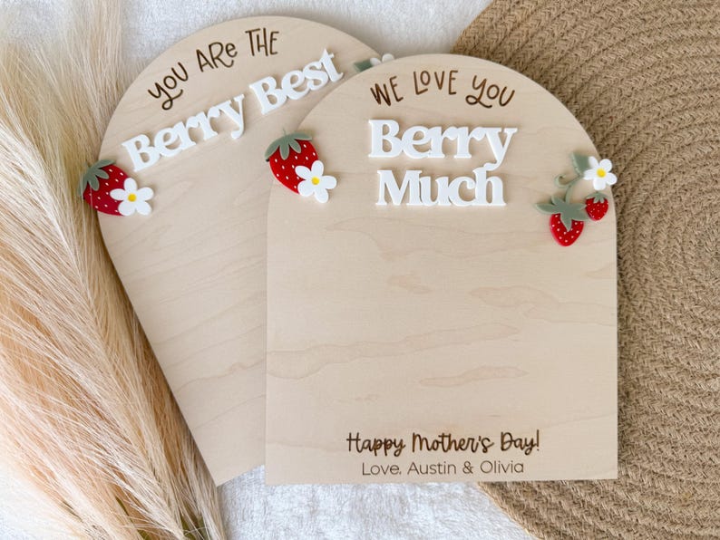 May include: Two wooden arch-shaped signs with the phrases "You Are The Berry Best" and "We Love You Berry Much" in white lettering. Each sign has strawberry and flower embellishments. The bottom sign reads "Happy Mother's Day! Love, Austin & Olivia."