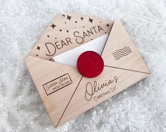Puede incluir: Sobre de madera con un sello de lacre rojo, decorado con estrellas y las palabras "Querido Santa". El sobre tiene una ranura para una carta y una etiqueta que dice "Correo de trineo Entrega especial". El sobre está personalizado con el nombre "Lista de Navidad de Olivia".