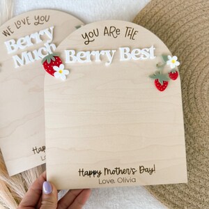 May include: Two wooden plaques with arched tops. One says "We love you Berry Much" and the other says "You are the Berry Best". Both have strawberry and flower embellishments. The bottom of the plaques say "Happy Mother's Day! Love, Olivia".