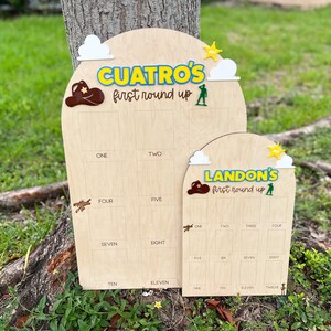 Peut inclure: Deux panneaux de suivi en bois en forme d'arche avec les inscriptions CUATRO'S FIRST ROUND UP et LANDON'S FIRST ROUND UP. Chaque panneau comporte des nuages blancs, une &eacute;toile jaune, un chapeau de cowboy marron et une figurine verte.