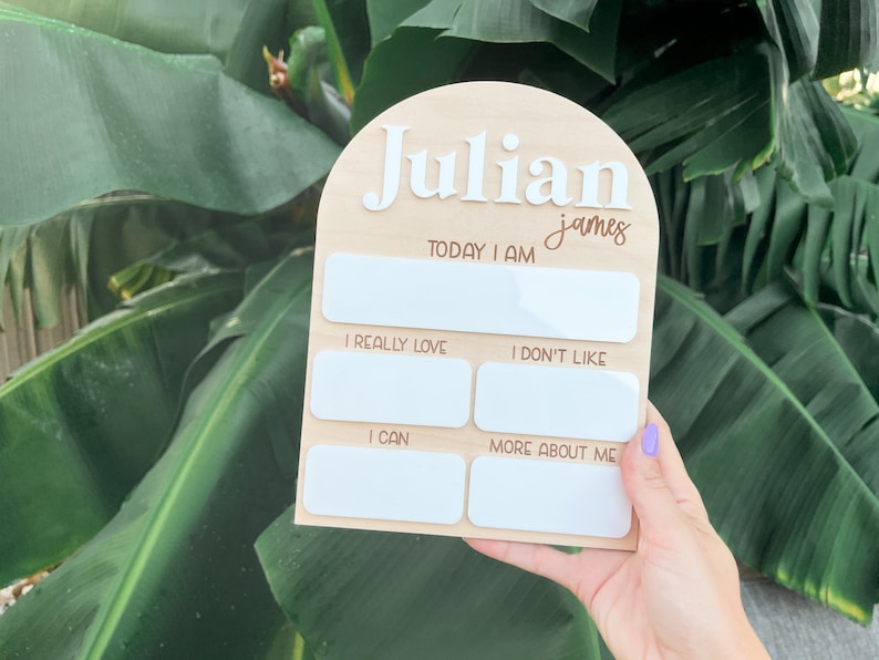 以下が含まれることがあります： 上部に白いアーチが付いた木製成長チャート。チャートには「Julian james」という名前が書かれています。チャートには、子供に関する情報を書き込むための空白のスペースが5つあります。スペースには、「今日は」「とても好き」「嫌い」「できる」「もっと私について」というラベルが付けられています。