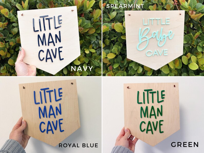 May include: Wooden pennant-shaped sign with the words "LITTLE MAN CAVE" in navy blue, royal blue, and green, and "LITTLE Babe CAVE" in spearmint. The signs are displayed against a background of greenery and a white wall.