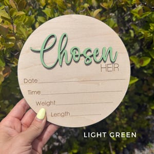 May include: A round wooden sign with the words "Chosen Heir" in light green script. The sign has lines for recording date, time, weight, and length. The text "LIGHT GREEN" is at the bottom.
