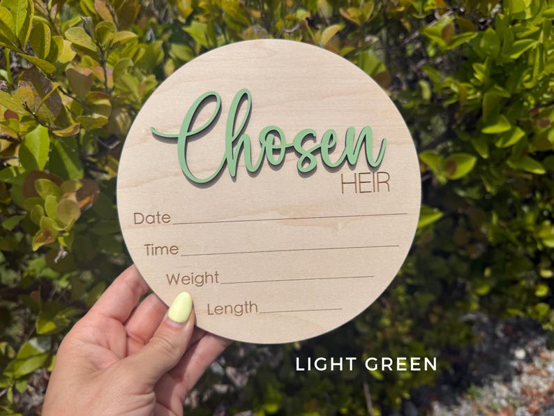 May include: A round wooden sign with the words "Chosen Heir" in light green script. The sign has lines for recording date, time, weight, and length. The text "LIGHT GREEN" is at the bottom.